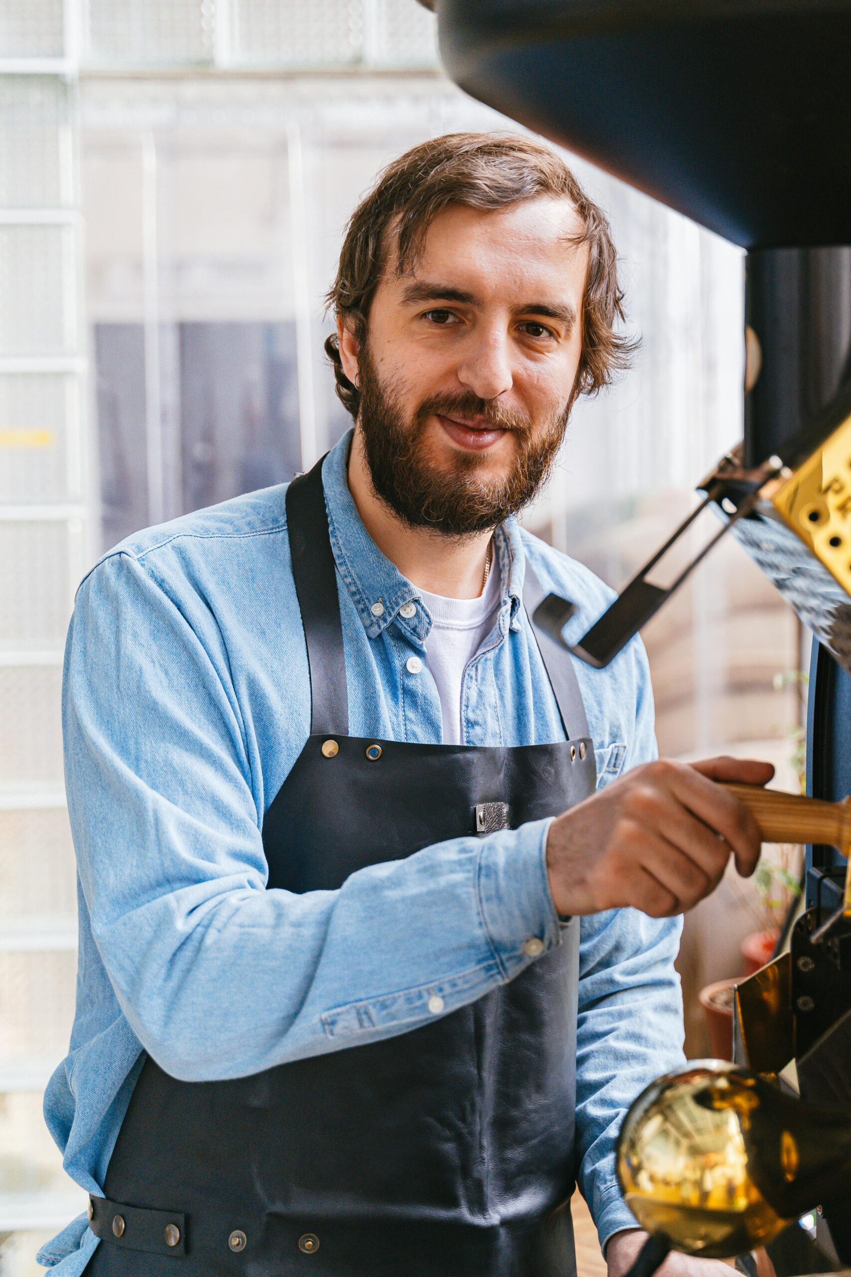 Friendly barista in apron using a coffee roasting machine with a smile indoors.